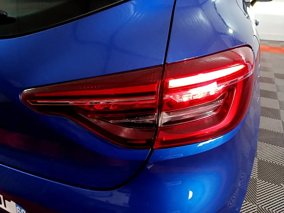 Gros plan sur le feu arrière droit rouge d'une Renault Clio Business bleu vif, avec carrosserie brillante et détails nets.