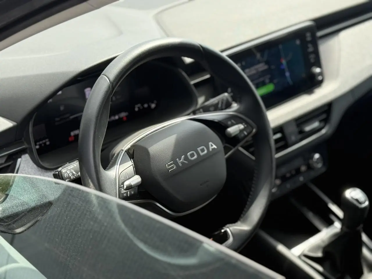 Vue intérieure rapprochée du volant en cuir noir et de la console centrale d’une Skoda Scala TSI 116 gris graphite.