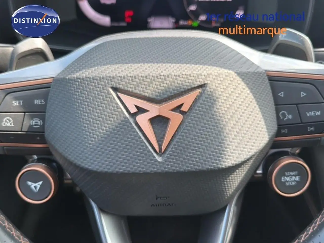 Gros plan sur le volant au design texturé avec logo CUPRA cuivré, boutons multifonctions et démarrage moteur.