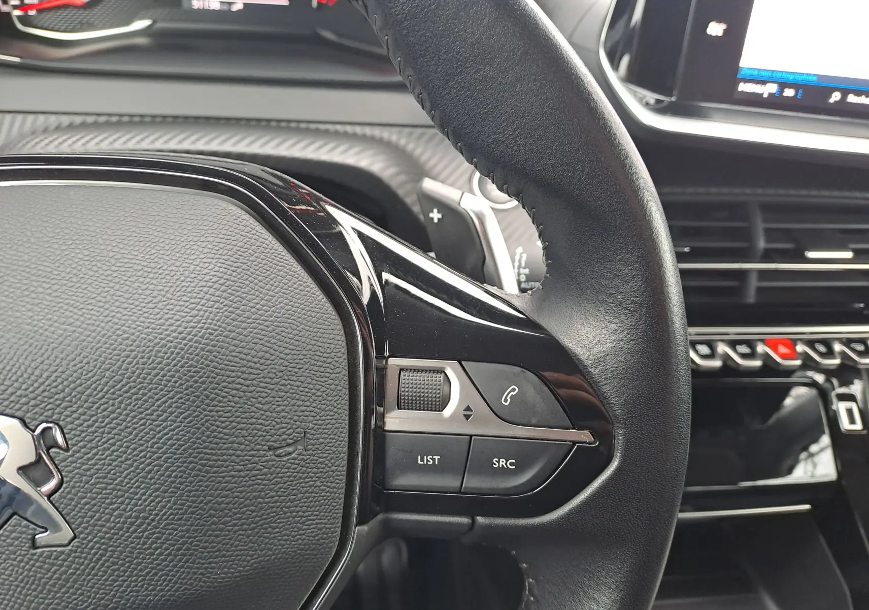 Gros plan sur le volant noir du Peugeot 2008 2020 avec commandes audio et téléphone intégrées, tableau de bord en arrière-plan.