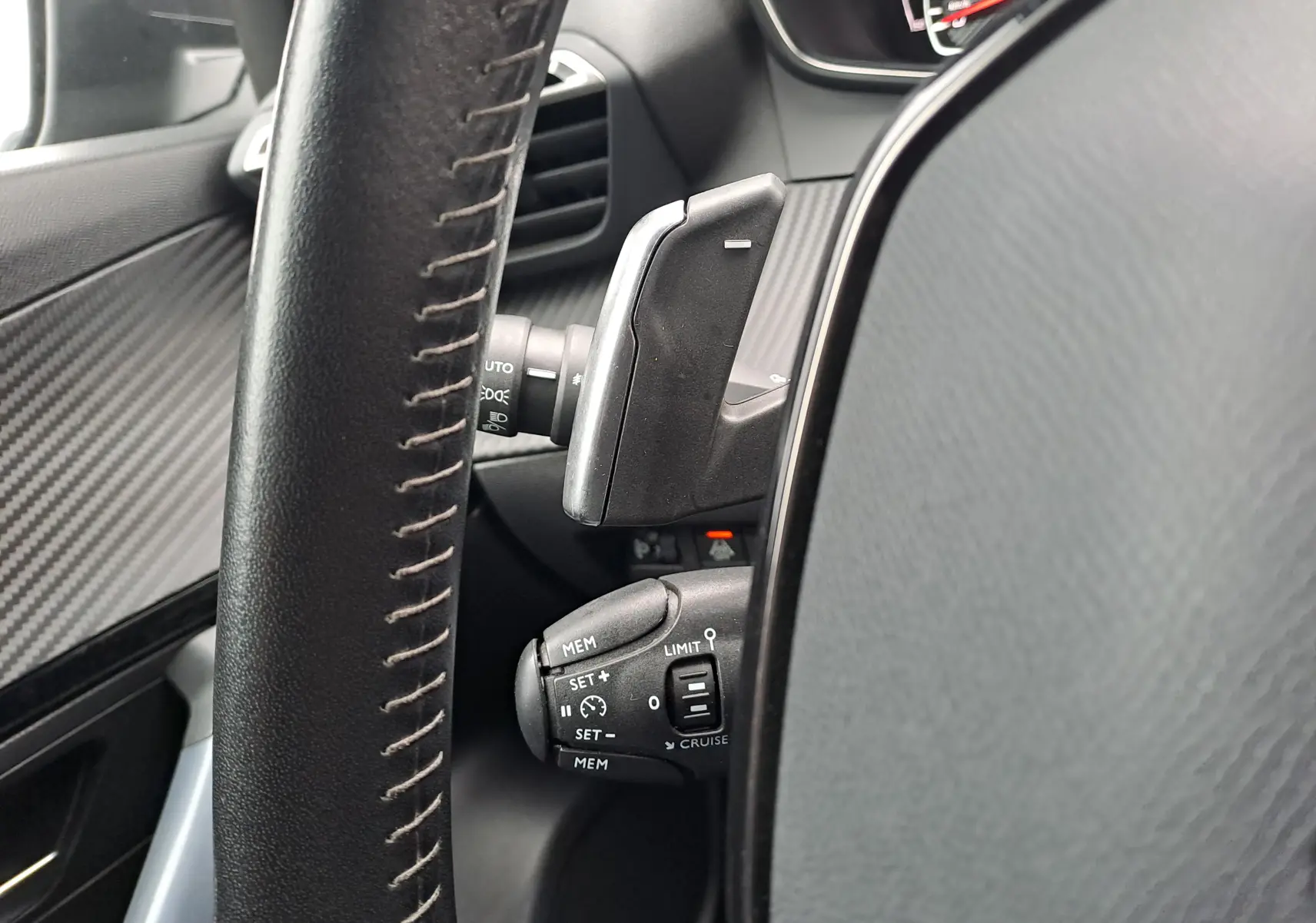 Gros plan sur la commande de régulateur de vitesse et palettes au volant noir du Peugeot 2008 gris Artense 2020.