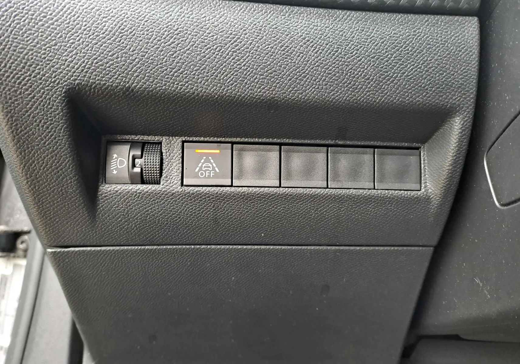 Gros plan sur les commandes de réglage des phares et désactivation de l'alerte de franchissement de ligne d'un Peugeot 2008 gris Artense 2020.