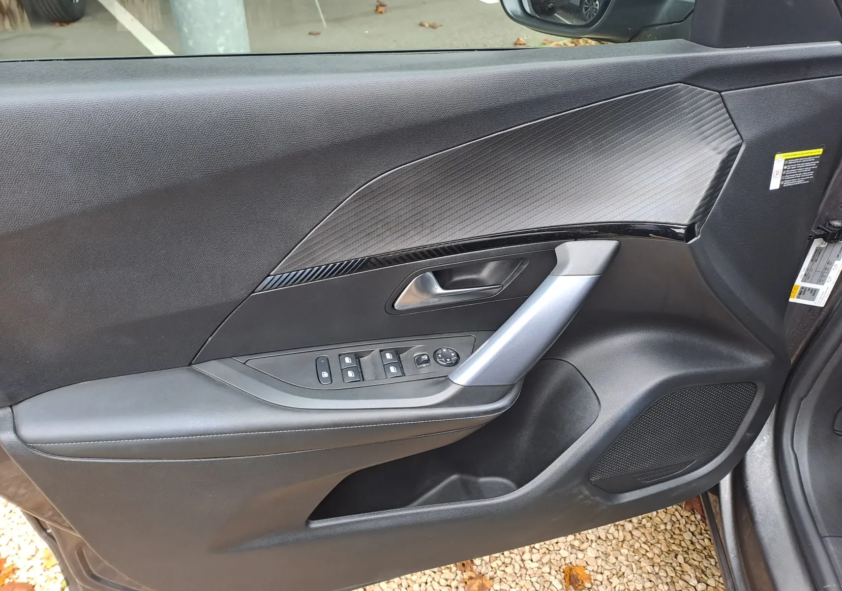 Intérieur de la porte avant gauche d'une Peugeot 2008 gris Artense, avec commandes électriques et insert décoratif noir.