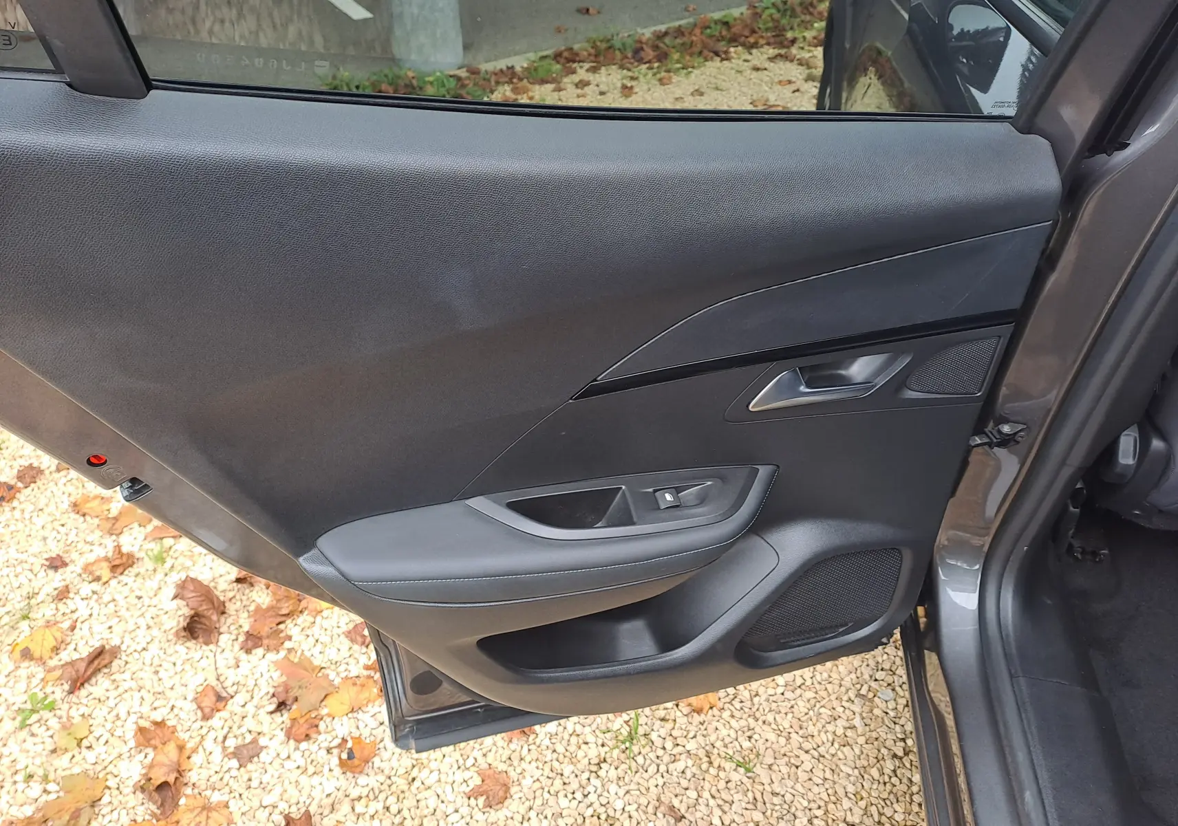 Porte arrière droite ouverte d'un Peugeot 2008 gris Artense, montrant la garniture intérieure noire avec commandes de fenêtre.