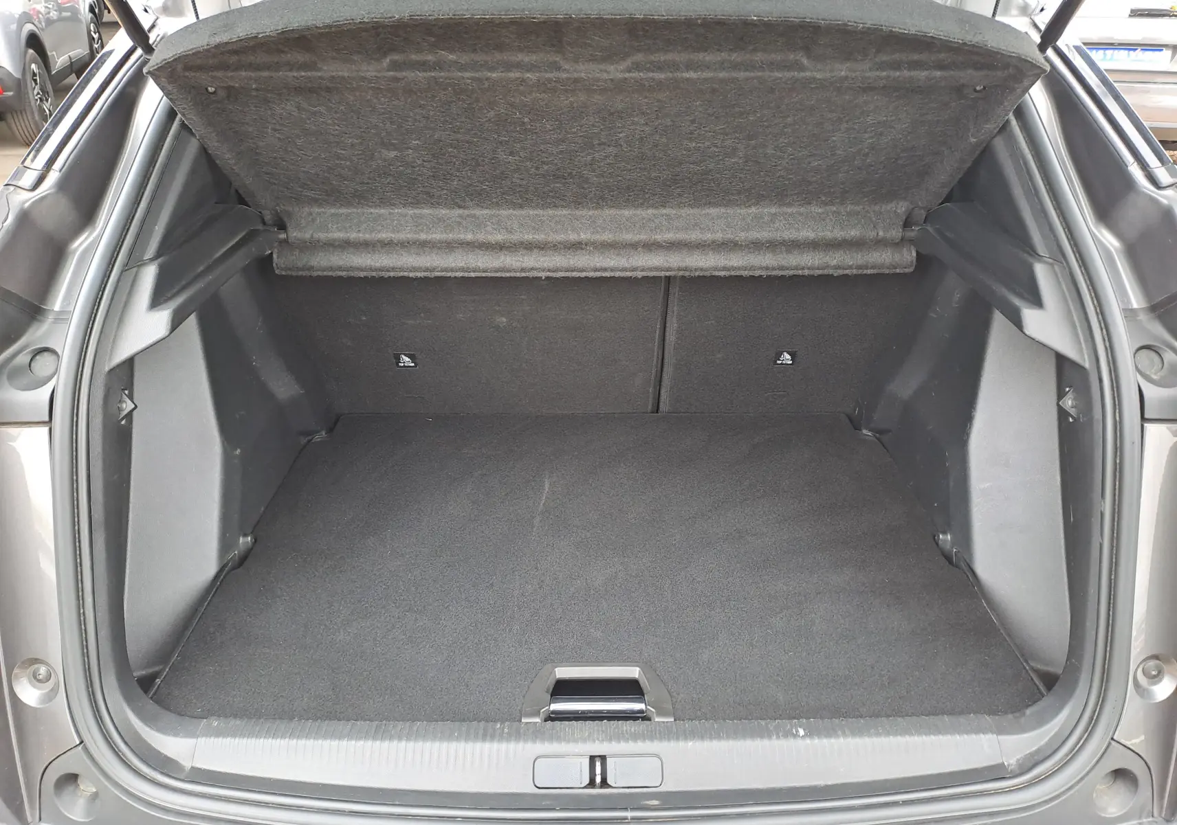 Coffre ouvert vu de l'arrière d'un Peugeot 2008 gris Artense, montrant l'espace de chargement vide et la tablette arrière relevée.