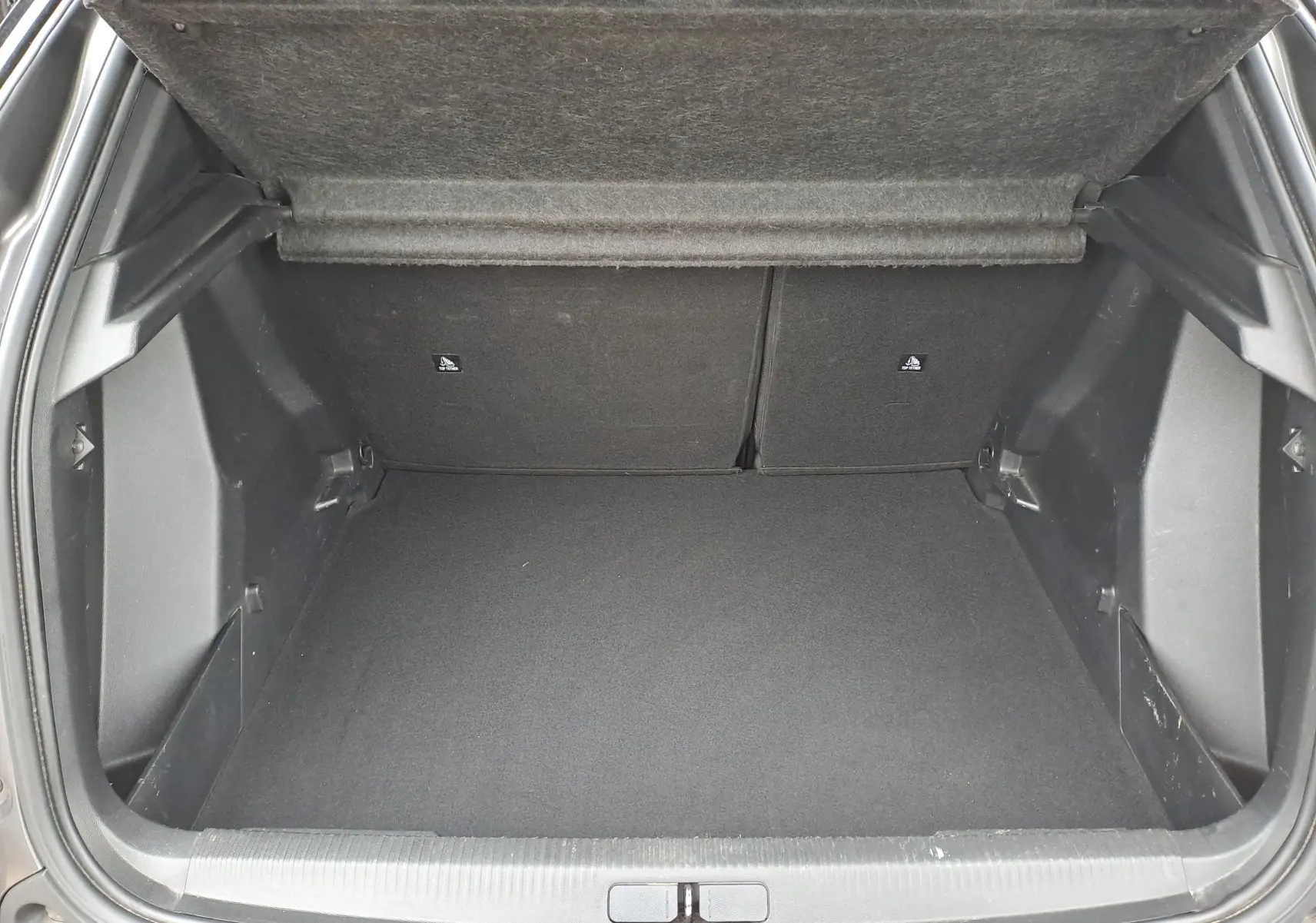 Coffre ouvert d'un Peugeot 2008 gris Artense, vue intérieure montrant l'espace de chargement vide et la tablette arrière relevée.