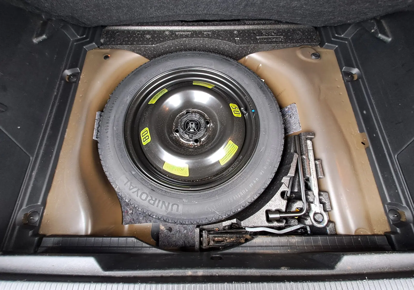 Roue de secours noire et outils de bord dans le coffre du Peugeot 2008 gris Artense, vue plongeante.