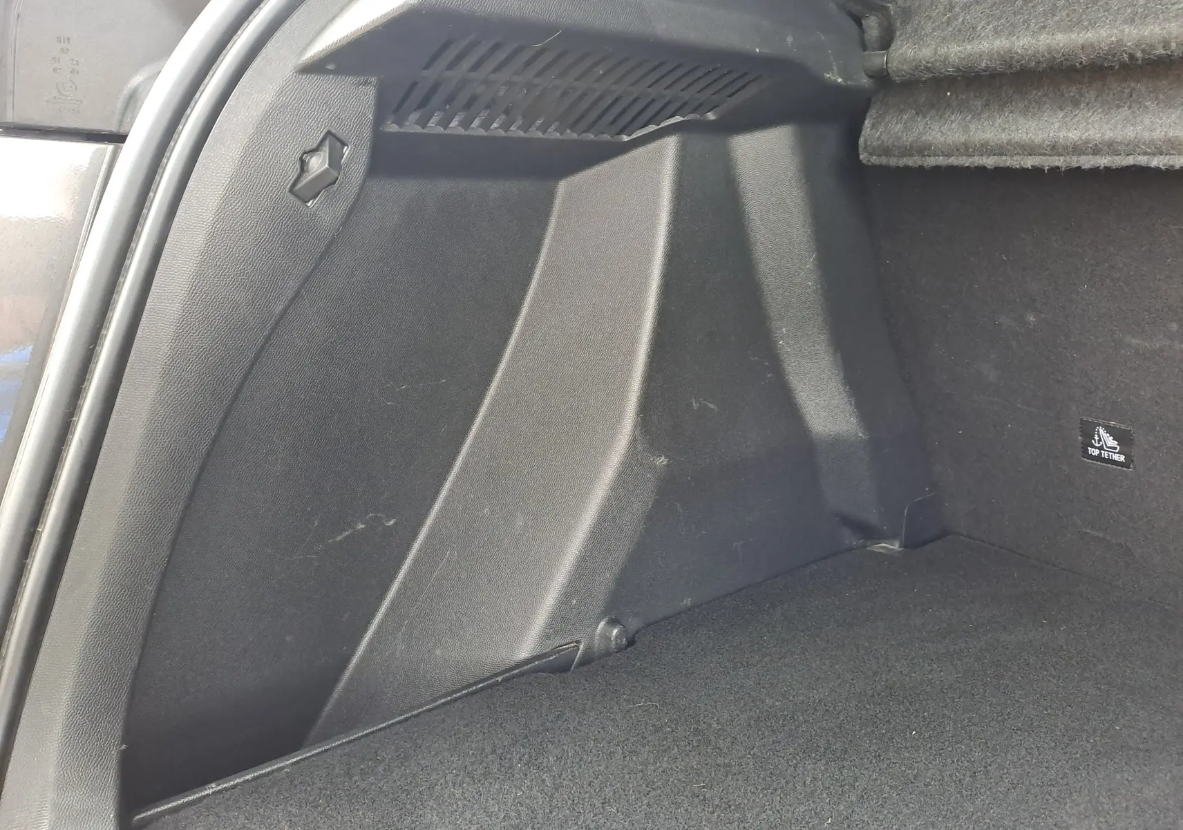 Détail de l'intérieur du coffre noir du Peugeot 2008 gris Artense, montrant la paroi latérale droite et l'attache Top Tether.