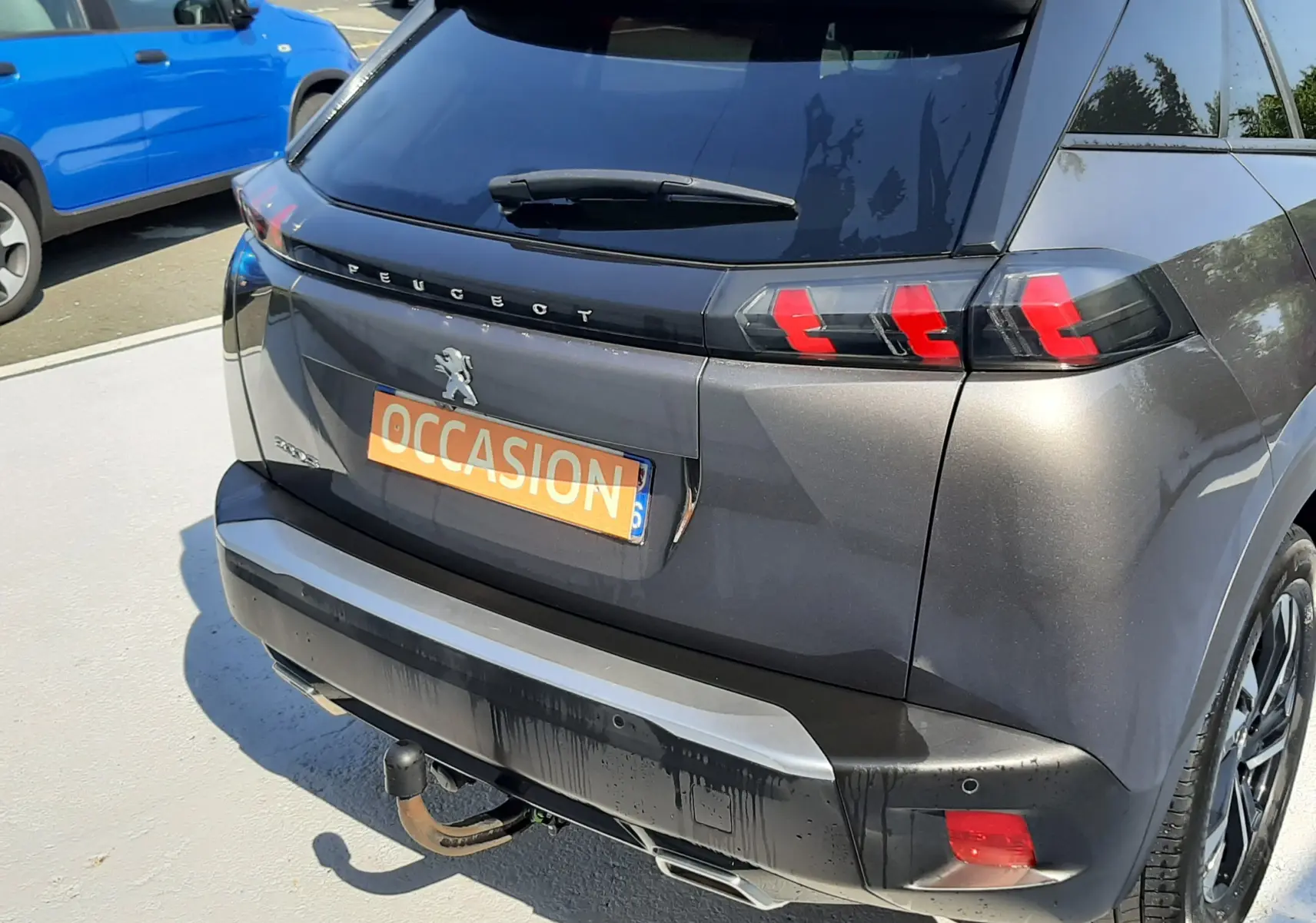 Vue 3/4 arrière droite d'un Peugeot 2008 gris Artense avec feux arrière LED et attelage visible sur parking.