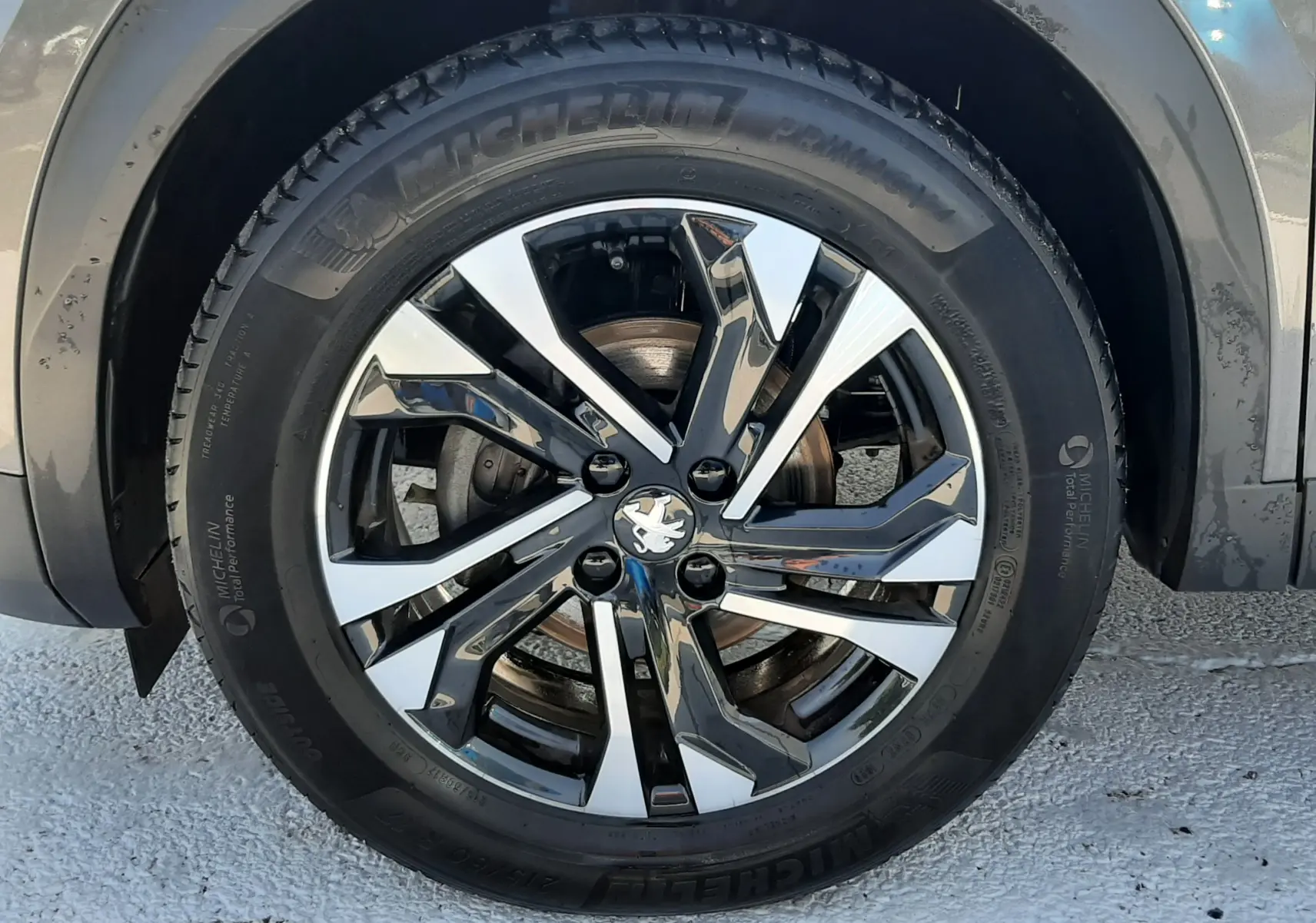 Gros plan sur la roue avant droite d'un Peugeot 2008 gris Artense avec jante alliage bicolore et pneu Michelin.