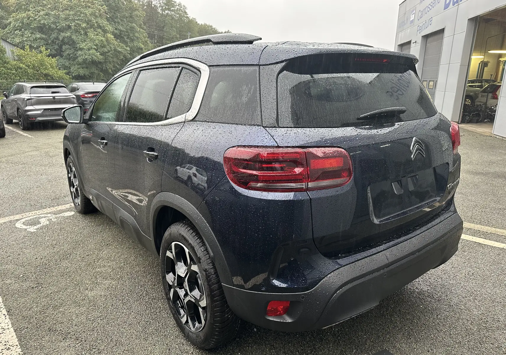 Vue 3/4 arrière droite d'un Citroën C5 Aircross Bleu Eclipse avec toit ouvrant et jantes alliage sous la pluie.