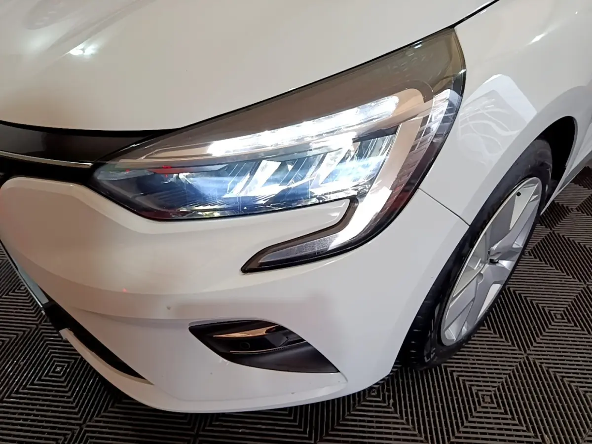 Gros plan sur l'avant droit blanc d'une Renault Clio 2020, mettant en valeur son phare LED et la jante alliage.