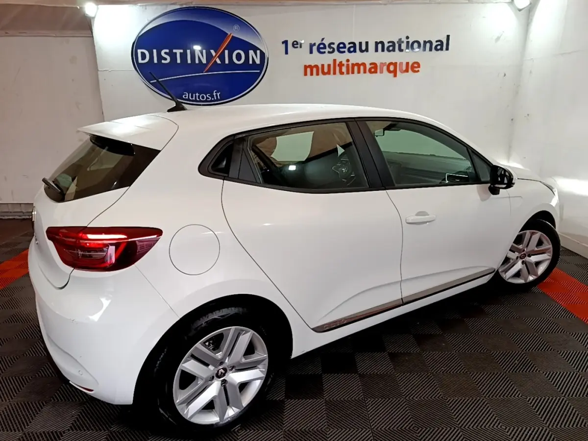 Vue 3/4 arrière droite d'une Renault Clio Business TCe 100 blanche, avec jantes alliage et feux arrière LED allumés.