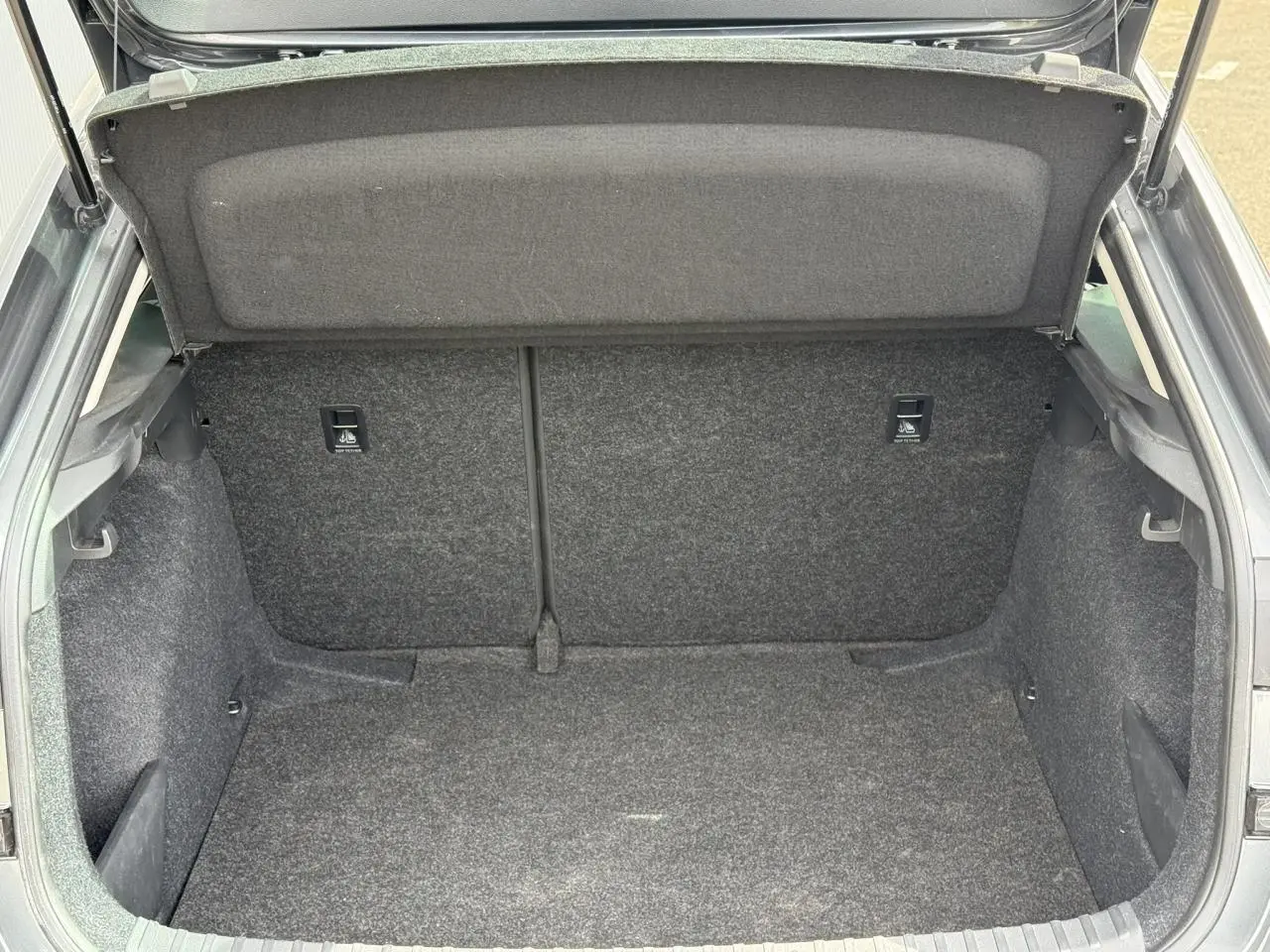 Coffre ouvert vu de l'arrière d'une Skoda Scala gris graphite, montrant l'espace de chargement vide et doublé de moquette.
