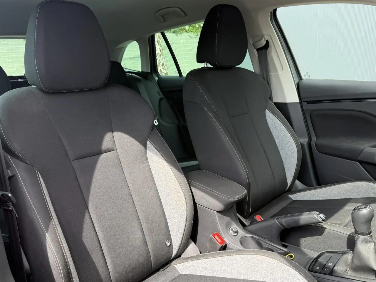 Vue intérieure des sièges avant tissu noir et gris avec accoudoir central et levier de vitesses d'une Skoda Scala TSI 116.
