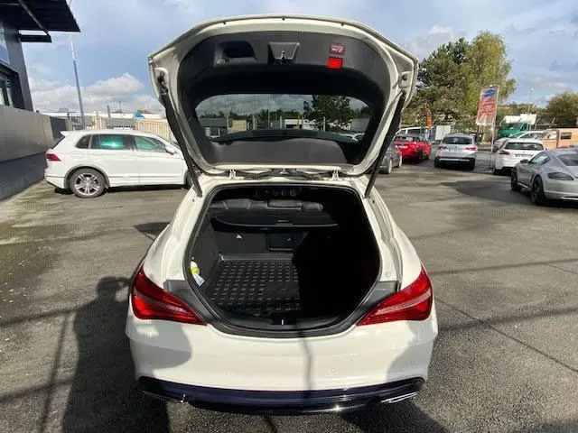 Vue arrière d'une Mercedes CLA Shooting Brake 200D WhiteArt Edition blanche avec coffre ouvert sur parking extérieur.