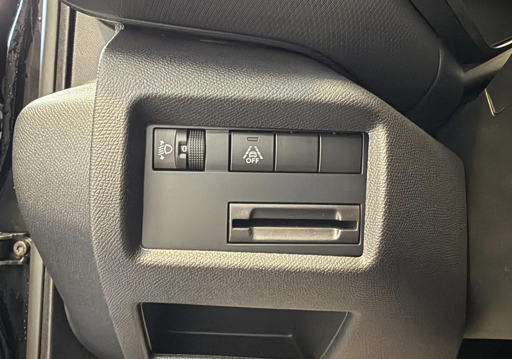 Gros plan sur les commandes de réglage des phares et d'aide à la conduite dans un Citroën C5 Aircross gris Artense 2022.