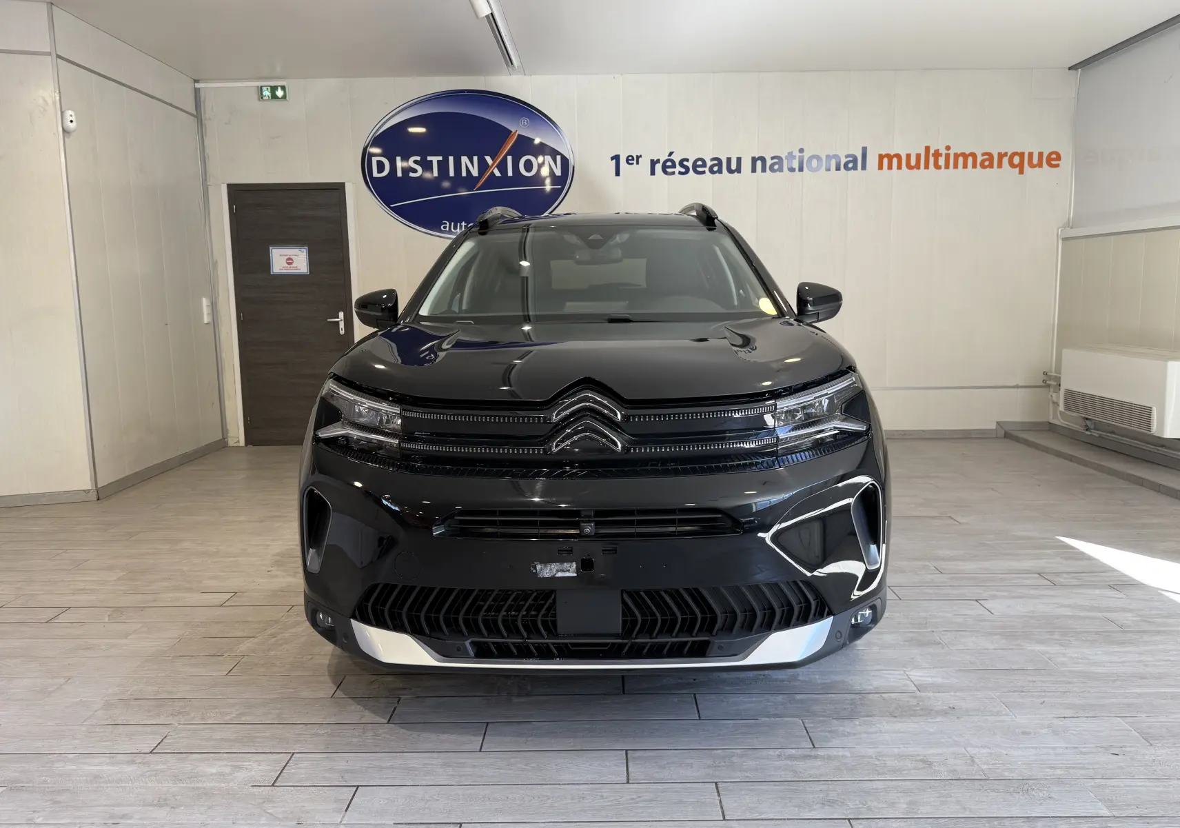 Vue frontale d'un Citroën C5 Aircross noir brillant avec calandre distinctive et éclairage LED dans un showroom.