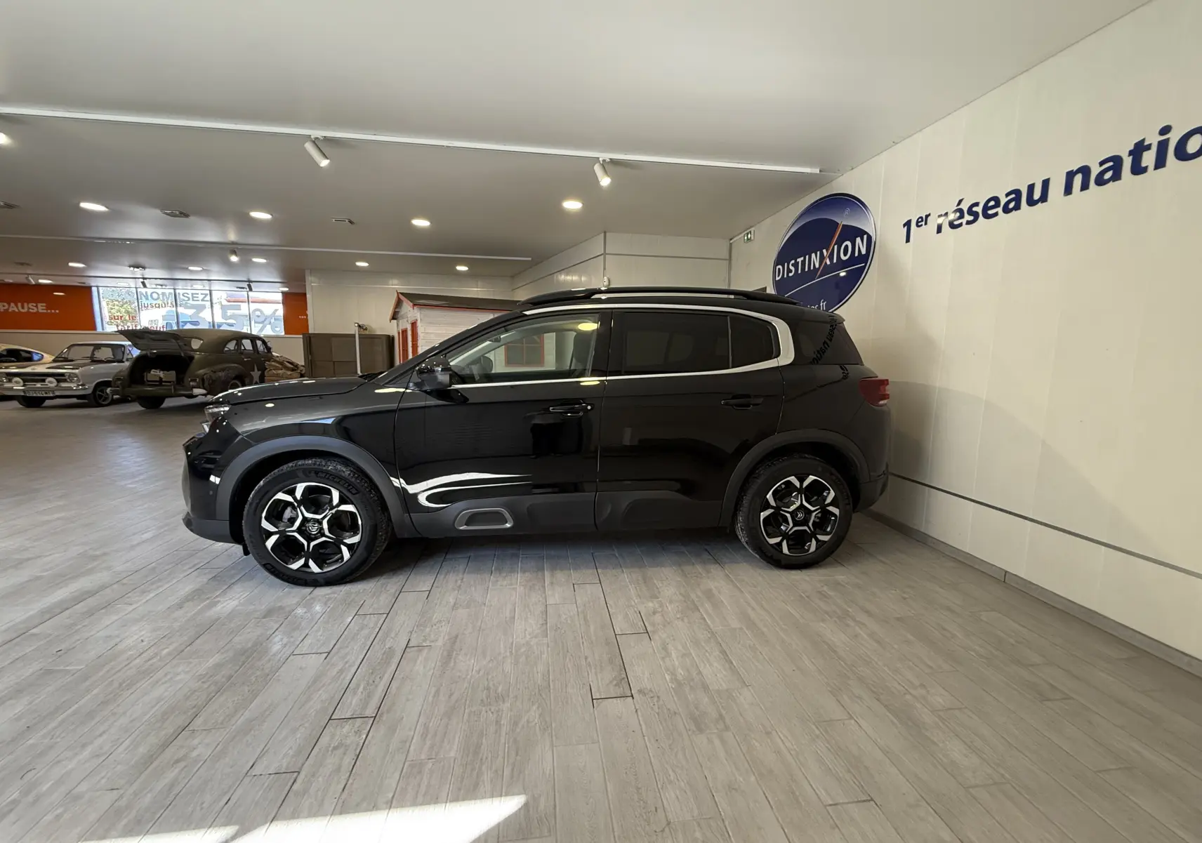 Vue de profil côté gauche d'un Citroën C5 Aircross gris Artense métallisé en showroom, avec jantes noires et détails chromés.