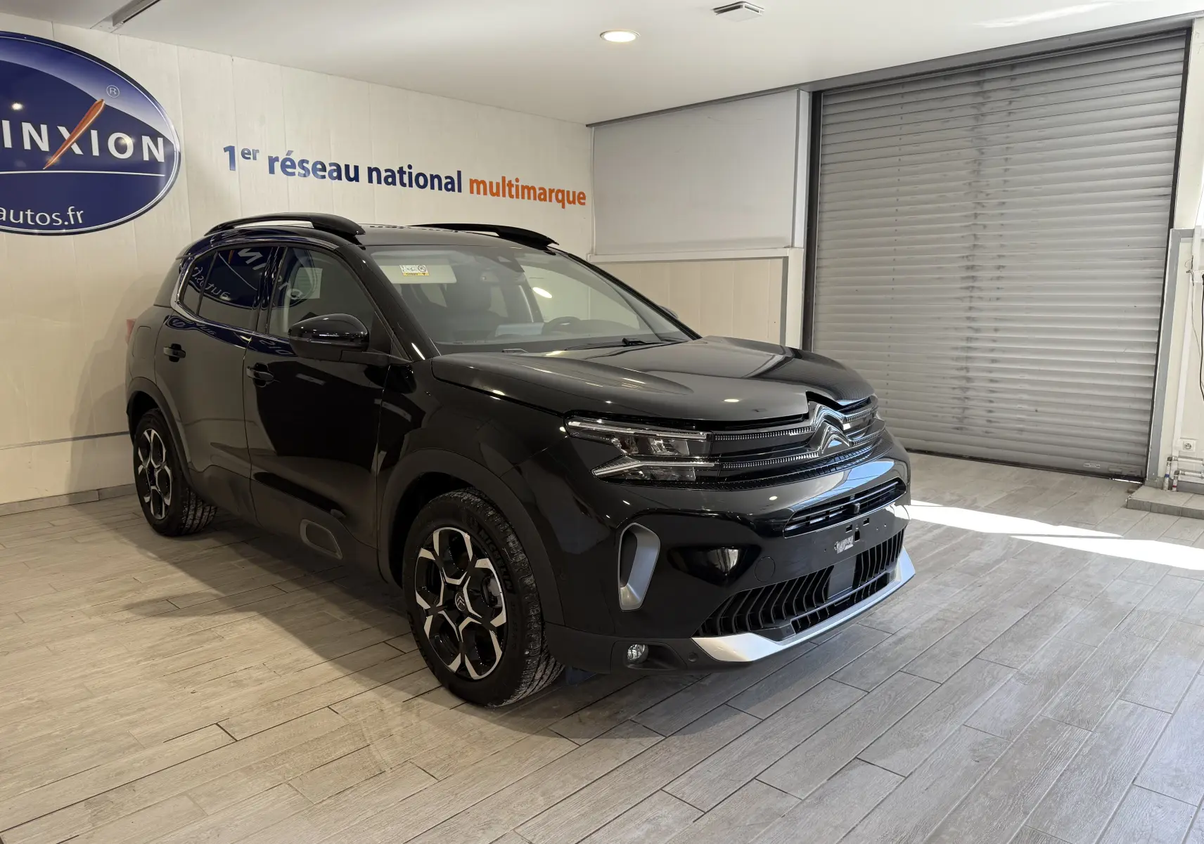 Vue 3/4 avant droite d'un Citroën C5 Aircross noir brillant en showroom, avec jantes distinctives et toit panoramique.