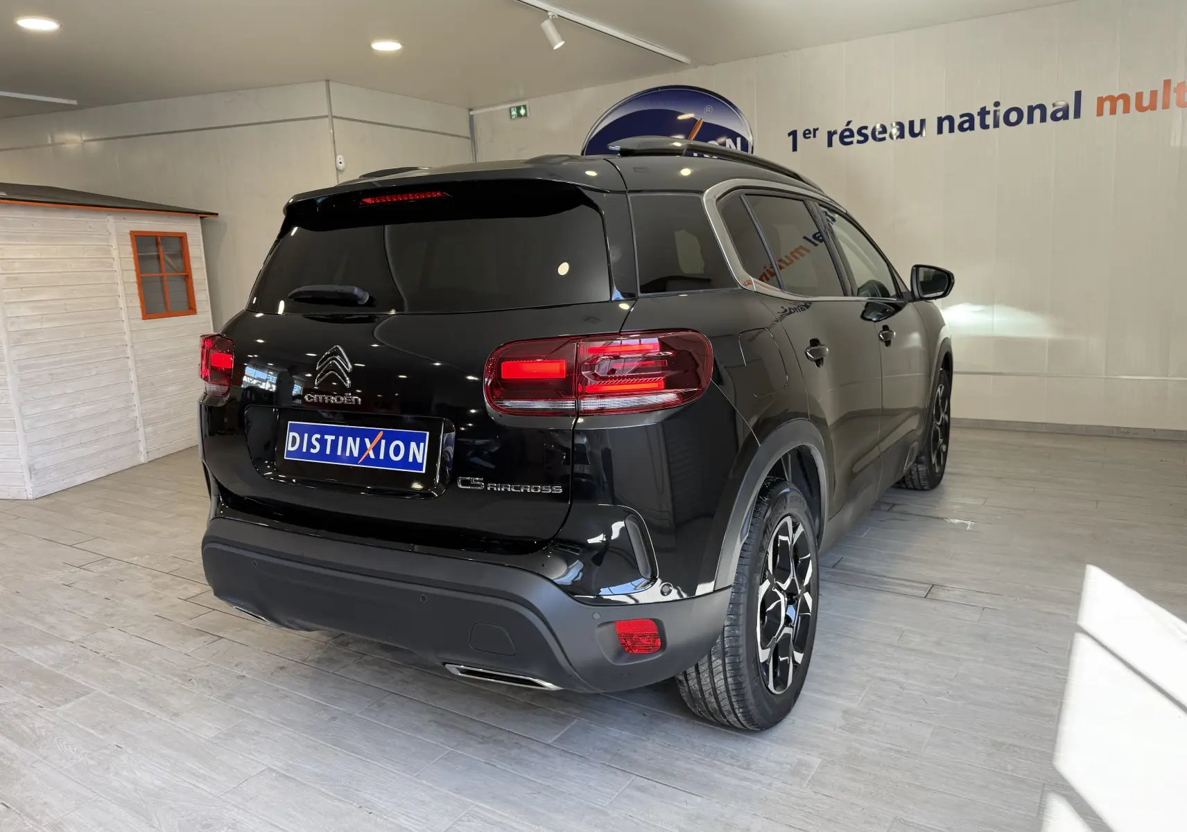 Vue 3/4 arrière droite d'un Citroën C5 Aircross noir brillant avec jantes alliage et feux arrière allumés en intérieur showroom.