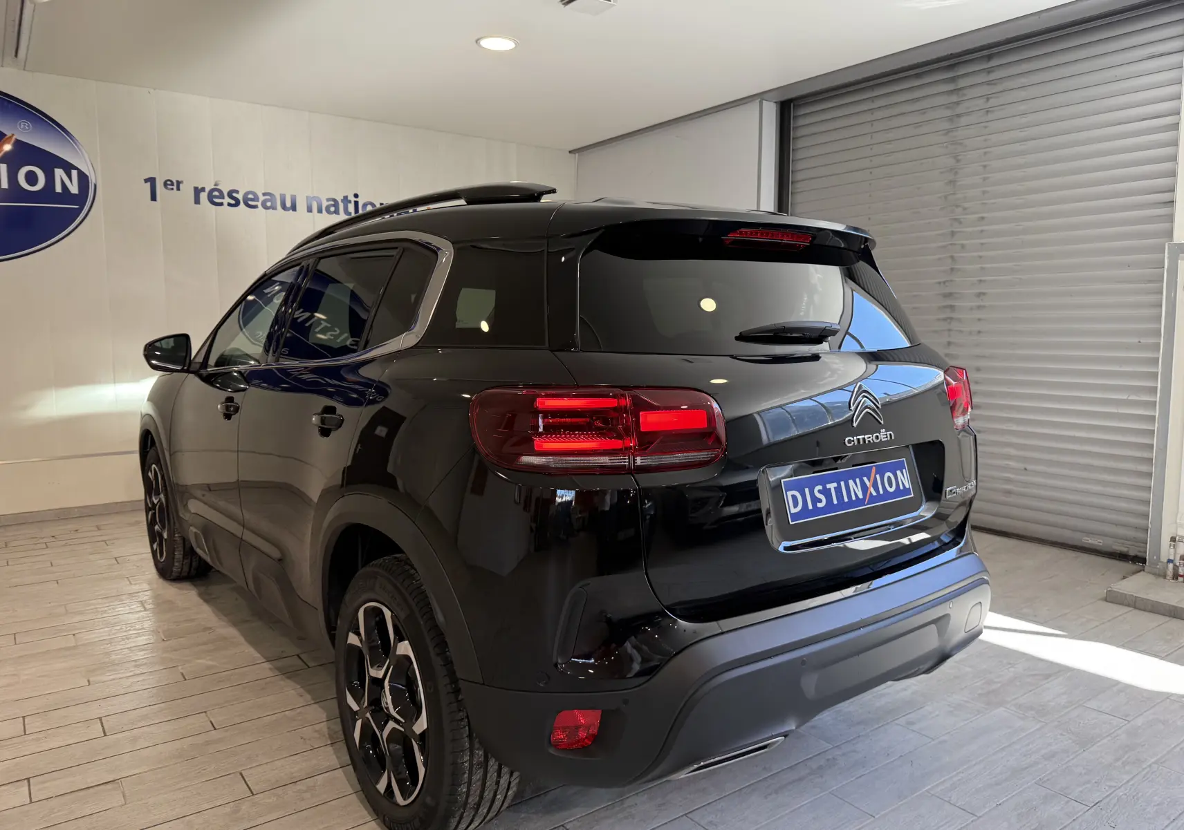 Vue 3/4 arrière droite d'un Citroën C5 Aircross noir brillant en showroom avec feux arrière allumés.