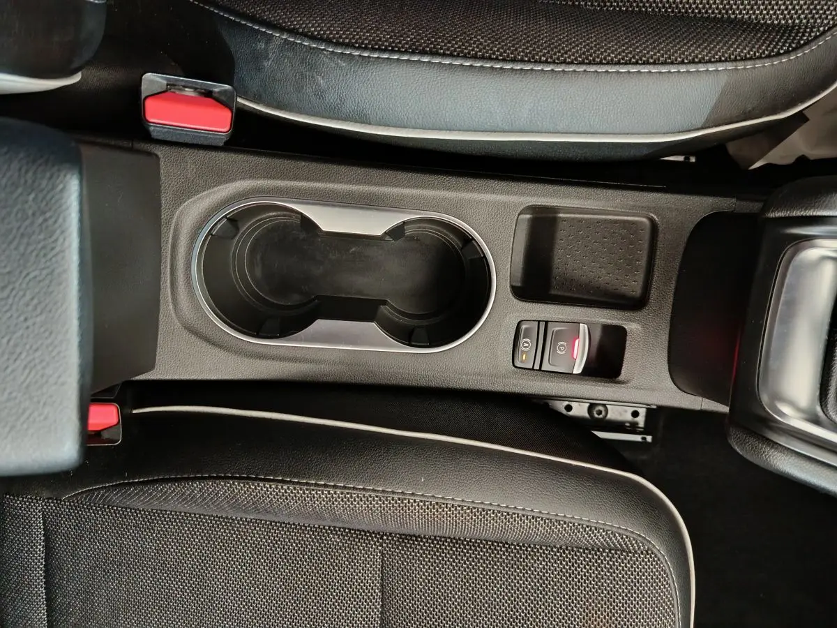 Gros plan sur la console centrale noire du Renault Captur 2024, avec porte-gobelets et bouton frein à main électronique.