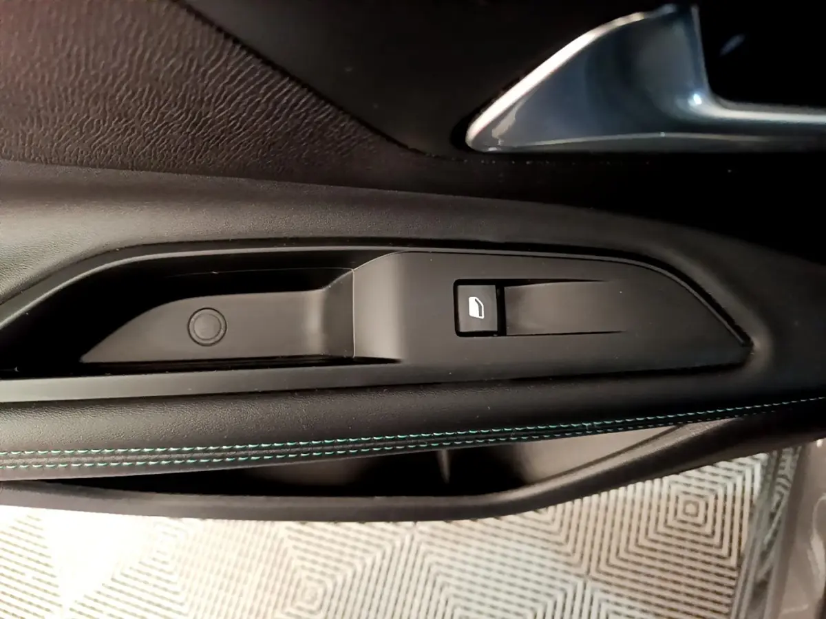 Gros plan sur la commande de lève-vitre côté conducteur avec surpiqûres bleues sur la garniture noire du Peugeot 3008 gris foncé.