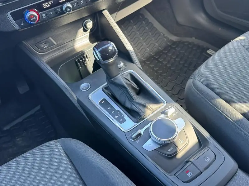 Vue rapprochée de la console centrale avec levier de vitesse automatique et commandes multimédia d'un Audi Q2 noir Mythic 2023.