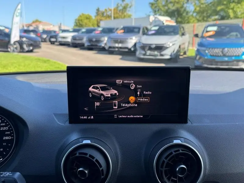 Écran central du tableau de bord d’un Audi Q2 35 TFSI S line 2023, avec vue sur l’interface multimédia et l’extérieur flou.