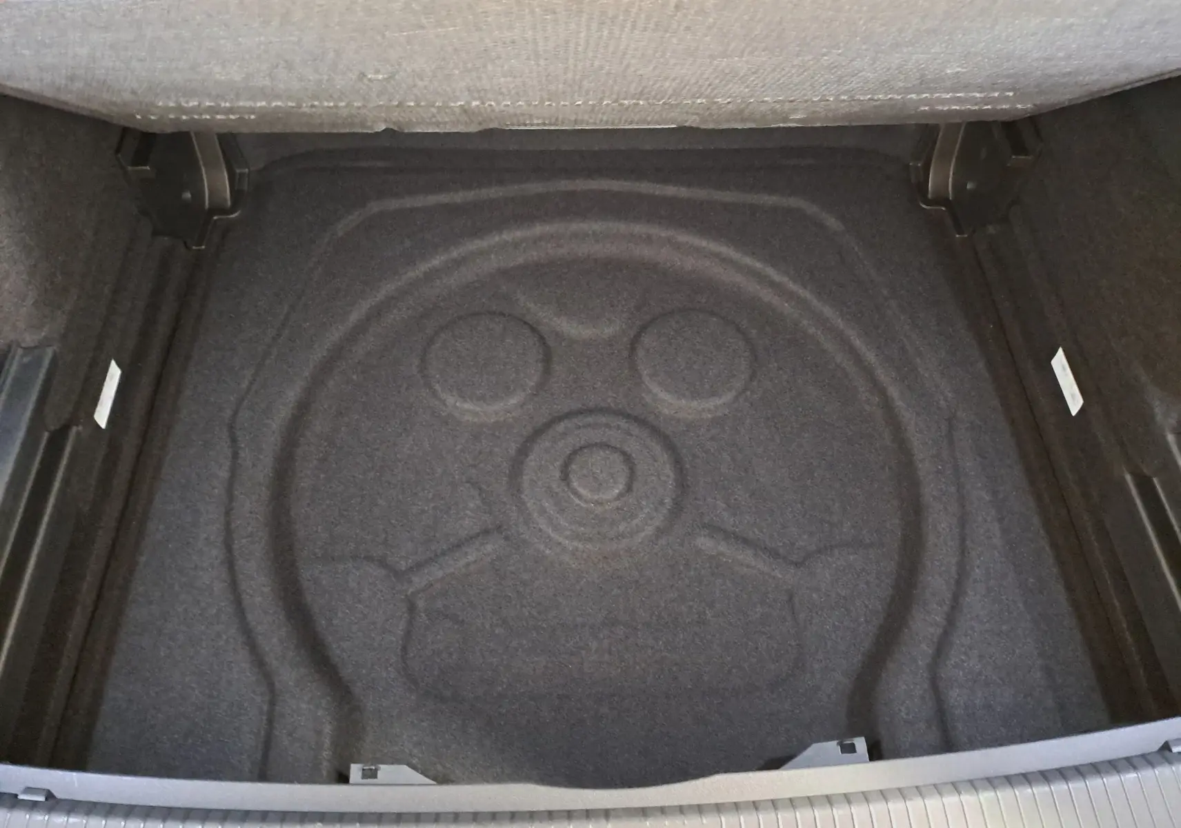 Vue plongeante sur le coffre vide du Volkswagen Tiguan 2.0 TDI 150 DSG7 R-Line, avec espace de rangement en moquette noire.