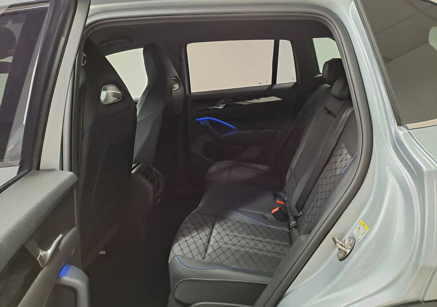 Vue intérieure côté gauche des sièges arrière en cuir noir avec surpiqûres et éclairage d'ambiance bleu du Volkswagen Tiguan 2025 argent Dolomite.