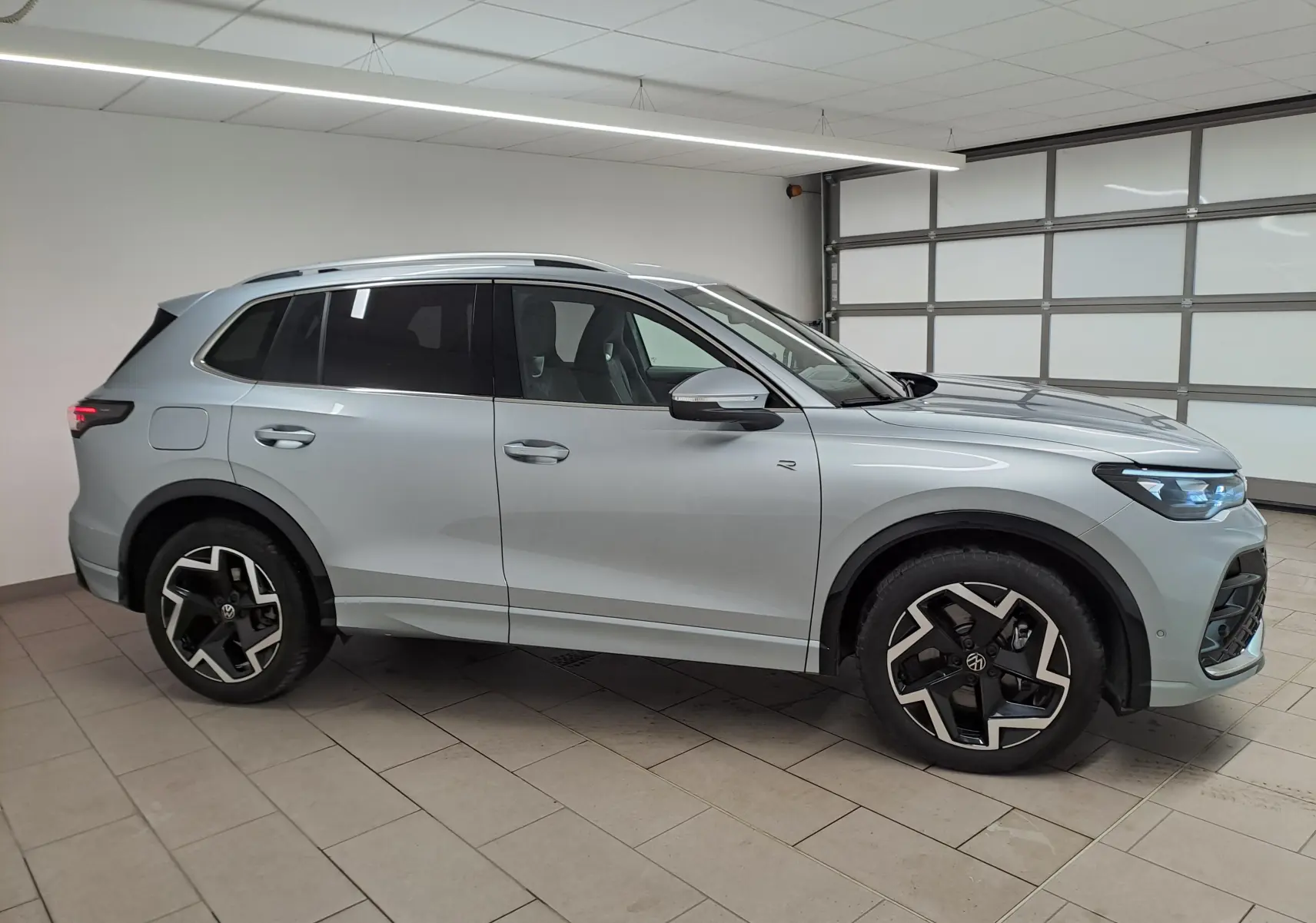 Vue de profil côté gauche d'un Volkswagen Tiguan 2.0 TDI R-Line argent Dolomite avec jantes noires et phares LED allumés.