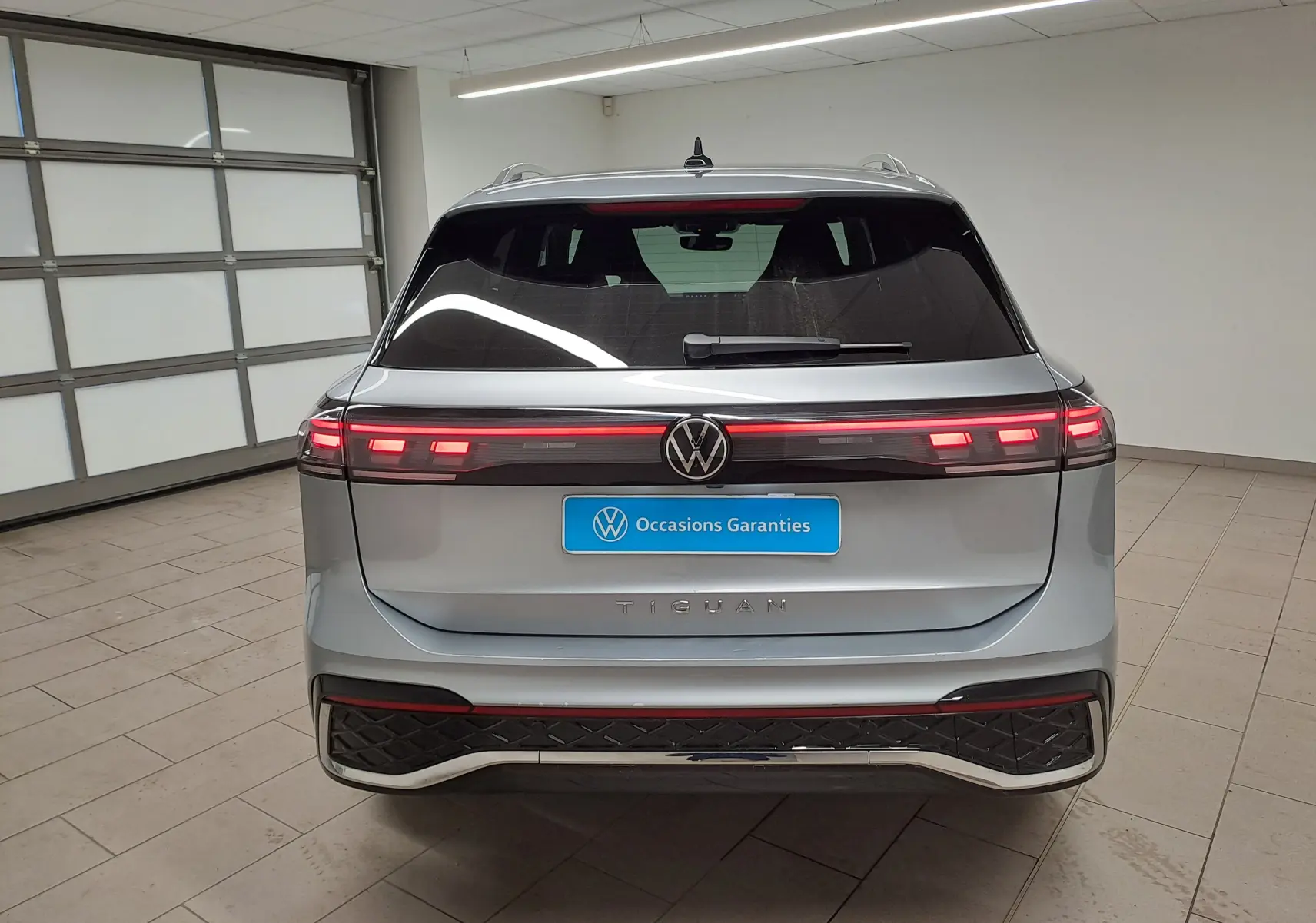 Vue arrière d'un Volkswagen Tiguan 2025 argent Dolomite avec feux LED allumés dans un garage intérieur.