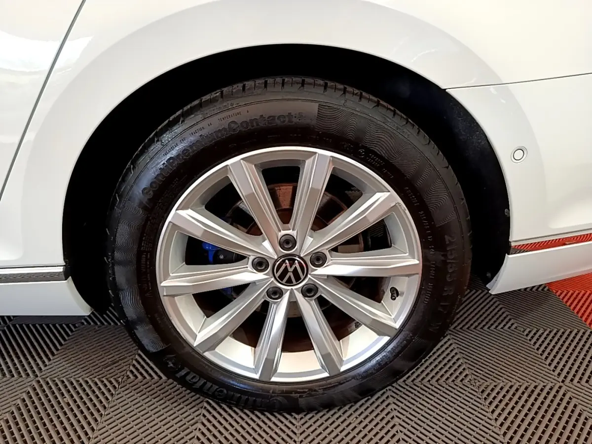 Gros plan sur la roue arrière droite d'une Volkswagen Passat blanche avec jante alliage et logo VW central.