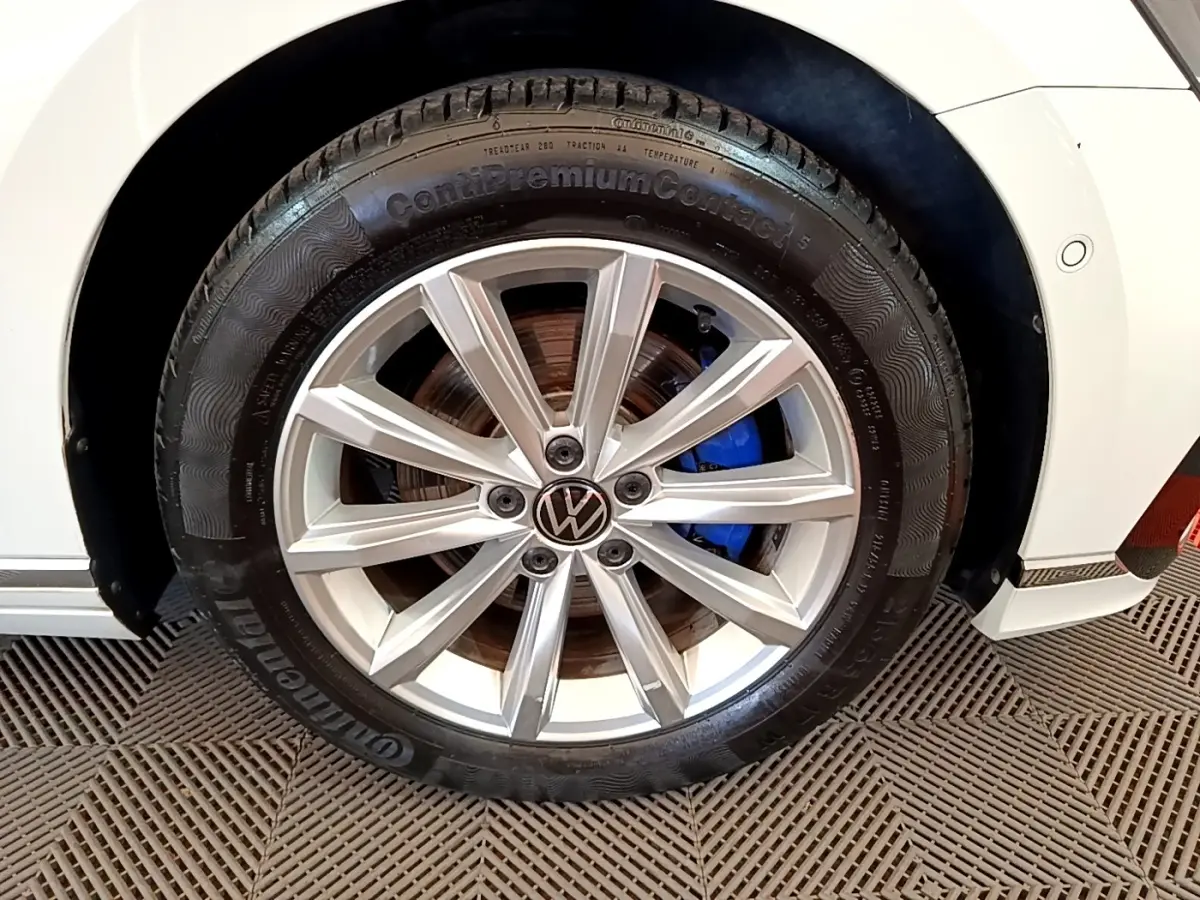 Gros plan sur la roue avant droite d’une Volkswagen Passat blanche avec jante alliage et étrier de frein bleu visible.