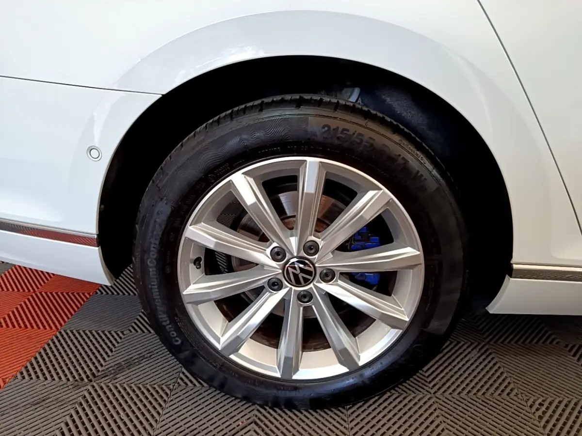 Gros plan sur la roue avant droite d'une Volkswagen Passat blanche avec jante alliage et étrier de frein bleu visible.