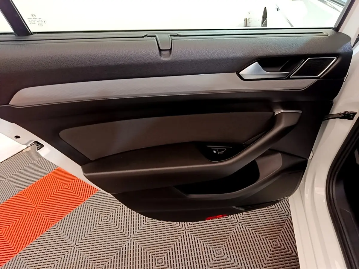 Vue intérieure de la porte avant droite noire et grise d'une Volkswagen Passat blanche, avec poignée et commande fenêtre.