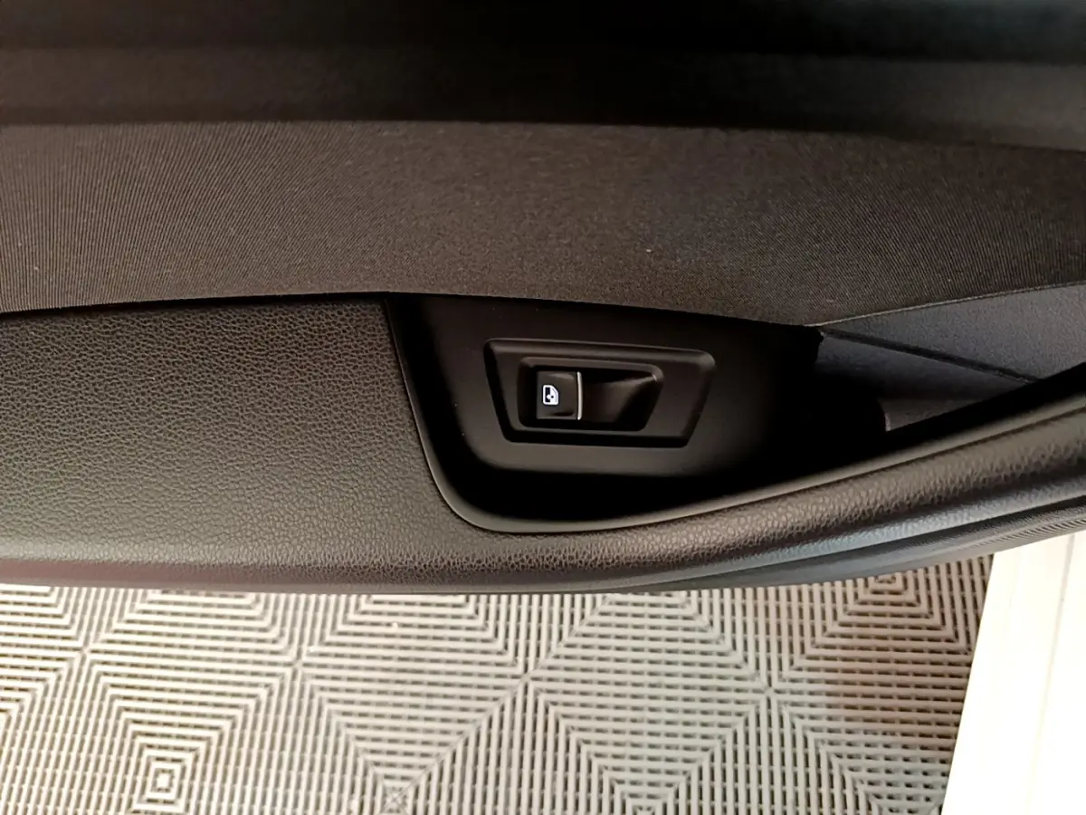 Détail du bouton d'ouverture électrique du coffre sur la porte intérieure d'une Volkswagen Passat blanche hybride rechargeable.