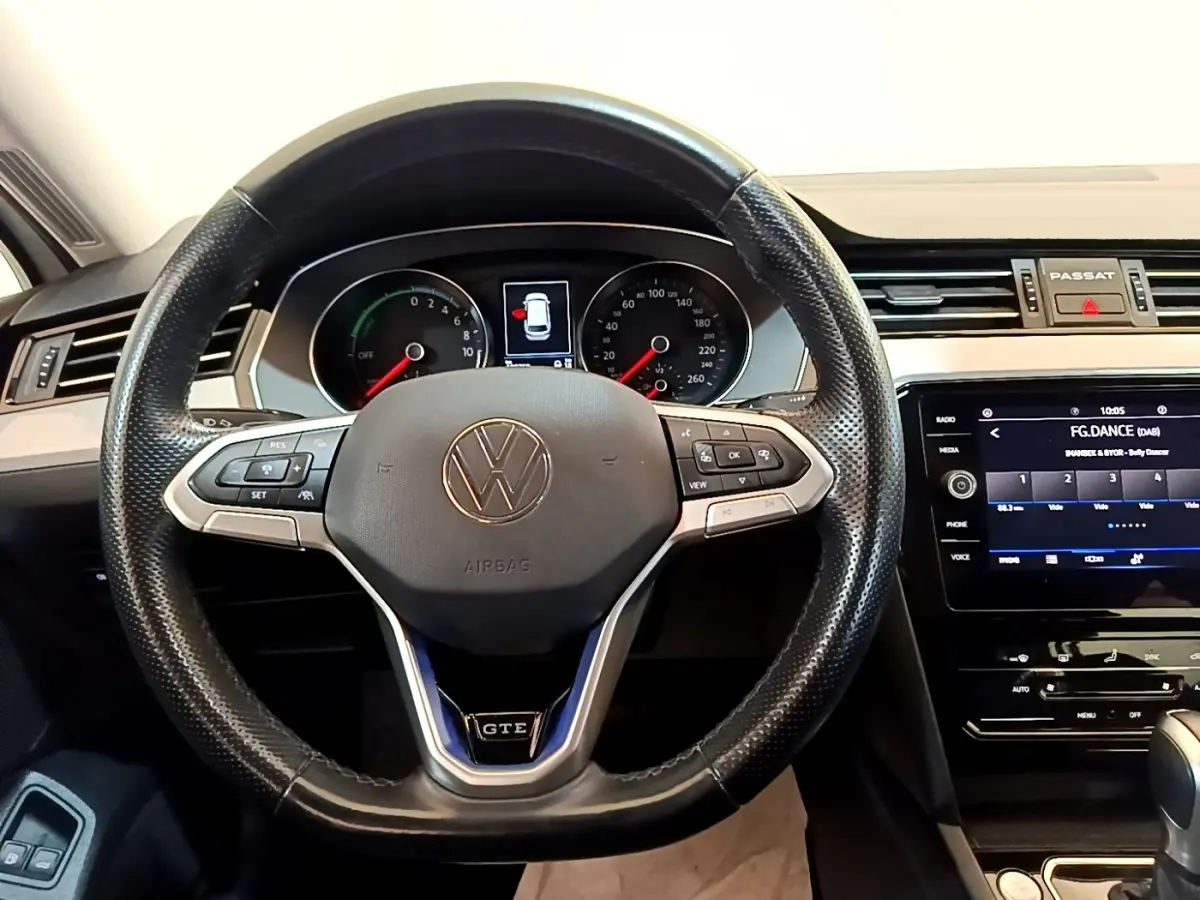 Vue intérieure centrée sur le volant cuir noir de la Volkswagen Passat GTE avec tableau de bord digital et écran tactile.