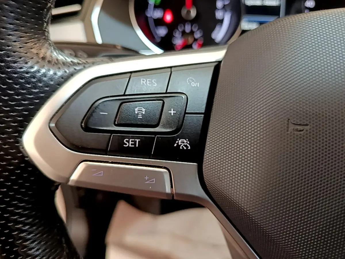 Gros plan sur les commandes de régulateur de vitesse au volant noir de la Volkswagen Passat hybride blanche.