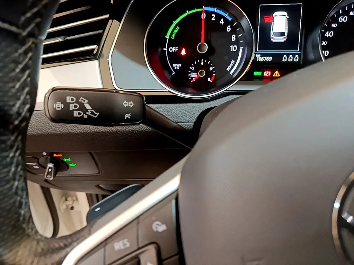 Vue rapprochée du tableau de bord et volant de la Volkswagen Passat hybride blanche, avec affichage digital et commandes au volant.