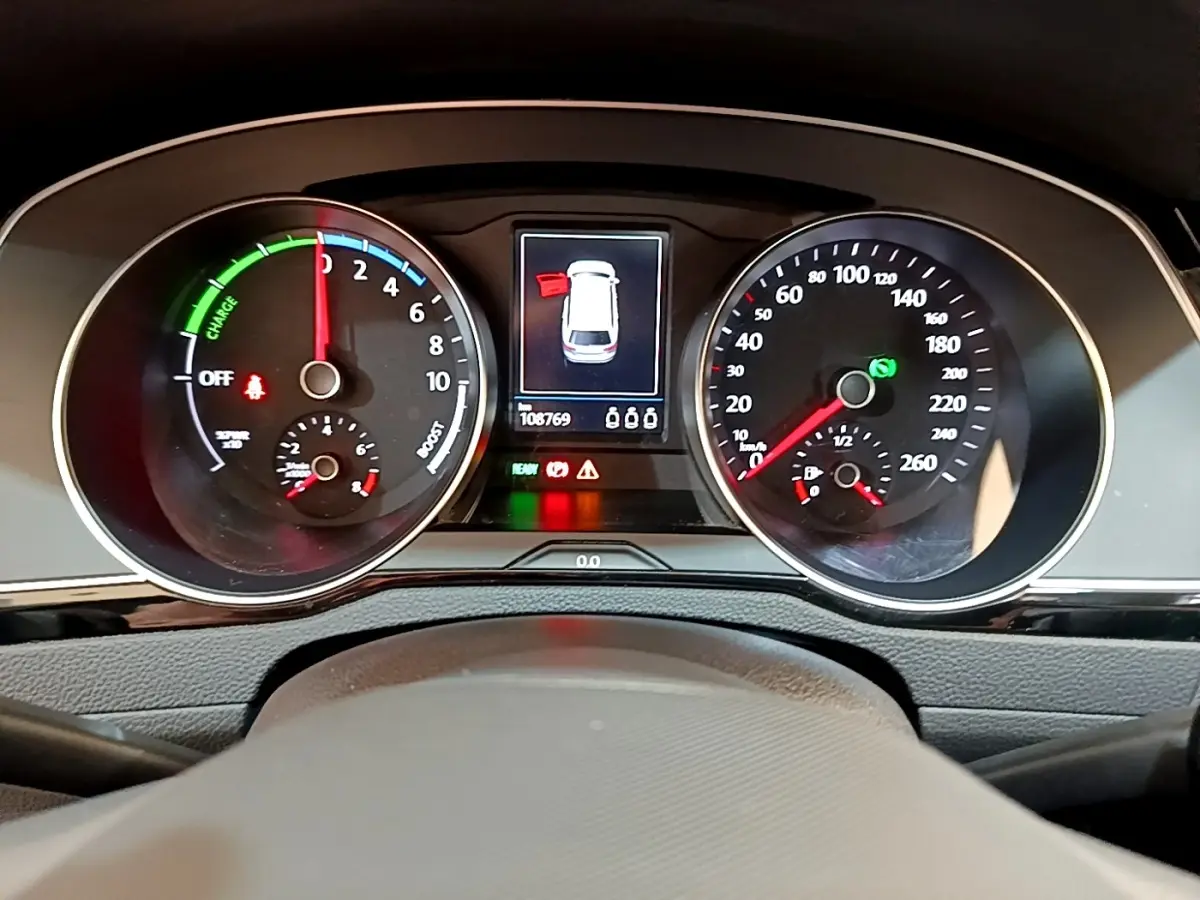 Vue rapprochée du tableau de bord digital de la Volkswagen Passat hybride blanche, affichant les compteurs et alertes.