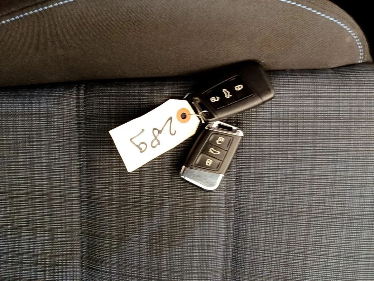 Clés de voiture Volkswagen Passat hybride posées sur un siège tissu gris à surpiqûres blanches.