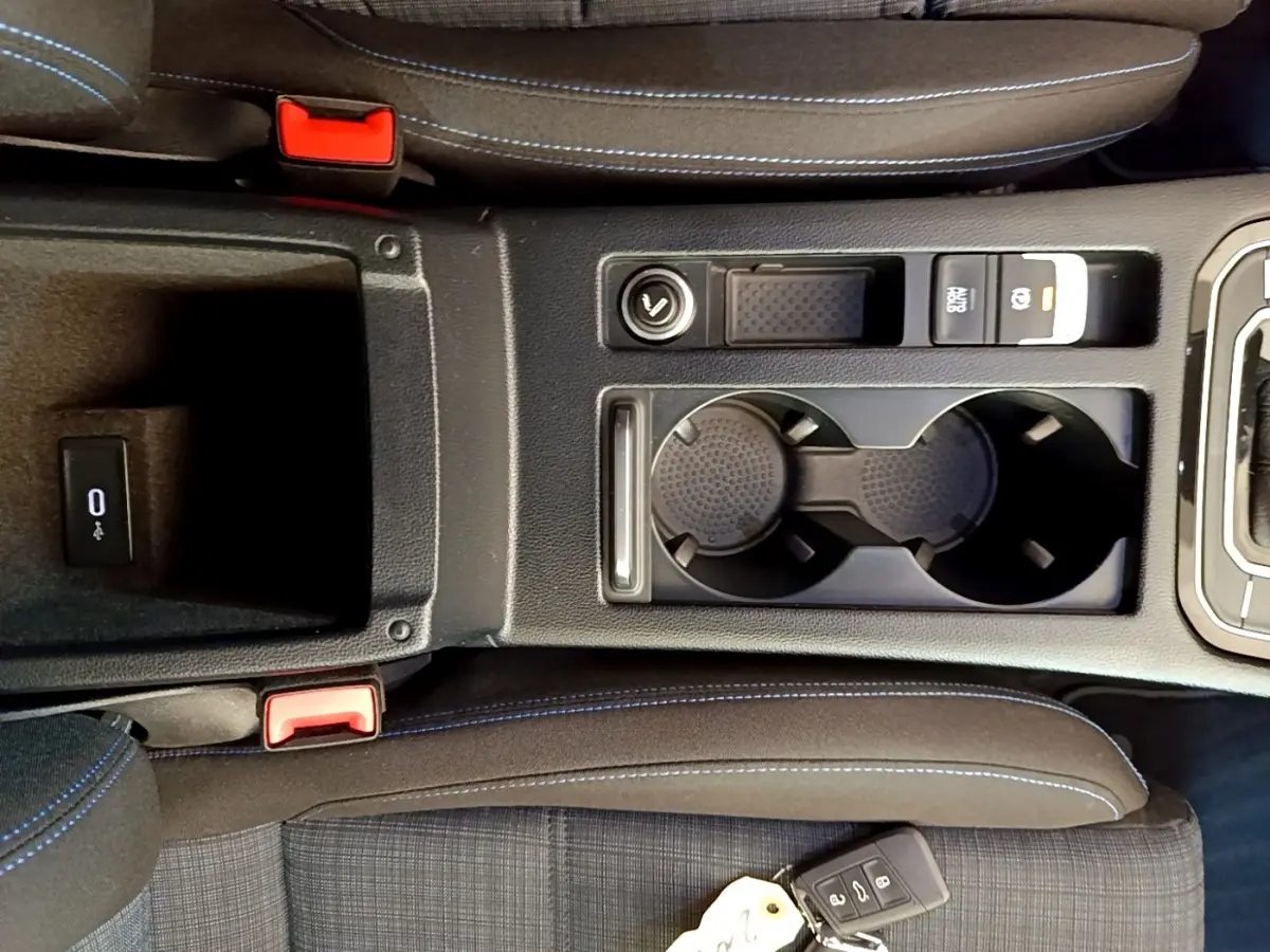 Vue plongeante sur la console centrale noire avec porte-gobelets et clé Volkswagen sur siège tissu gris à surpiqûres bleues.