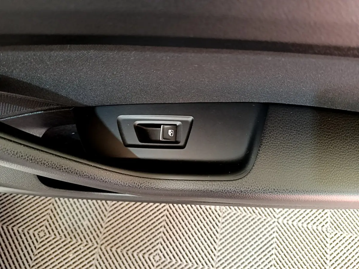 Gros plan sur le bouton d'ouverture électrique du coffre dans l'habitacle noir de la Volkswagen Passat hybride blanche.