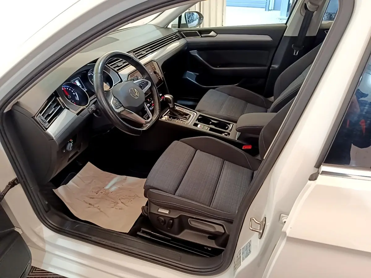 Vue intérieure côté conducteur d'une Volkswagen Passat blanche 2021, sièges tissu gris et tableau de bord digital.