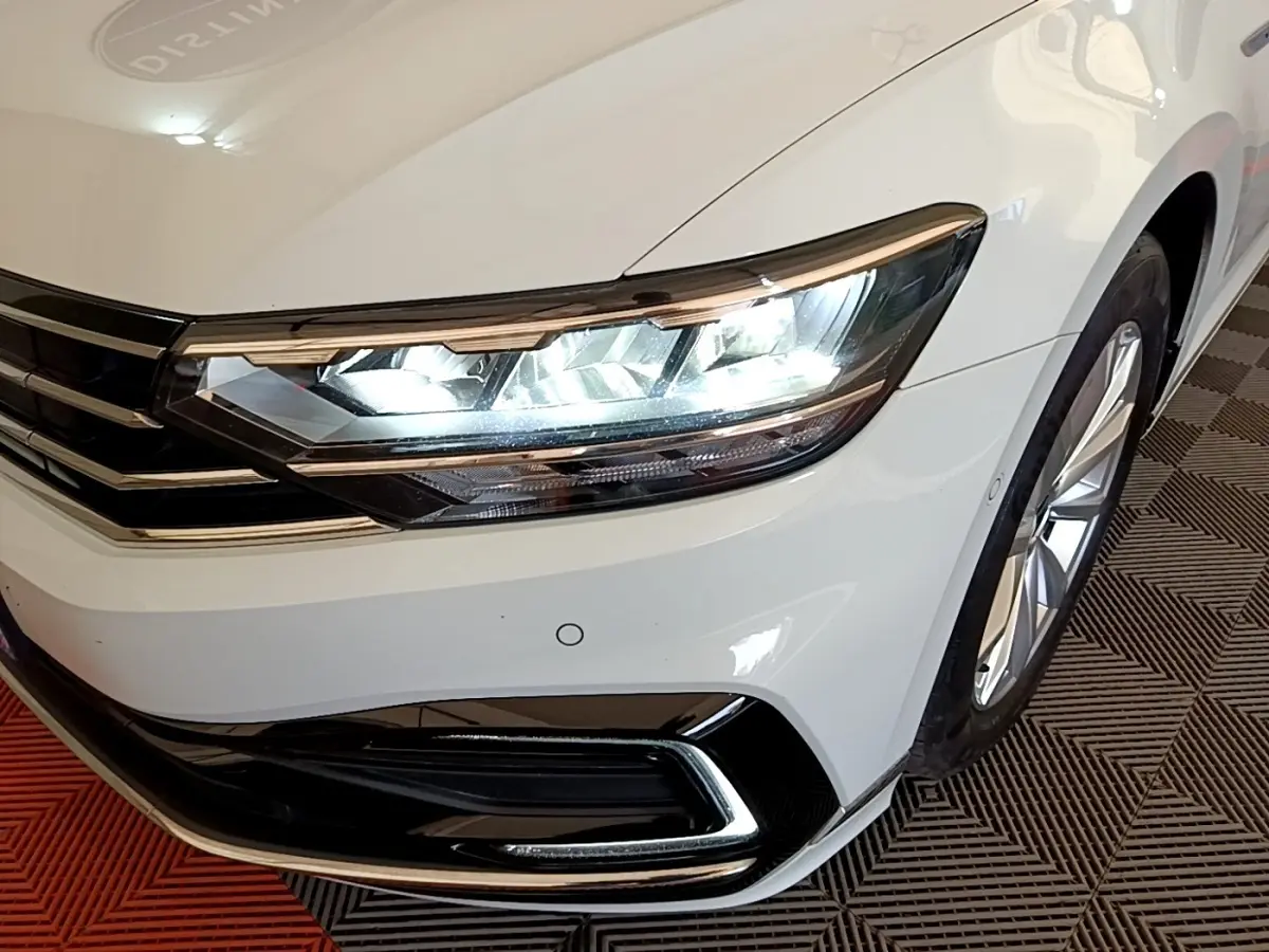 Gros plan sur l'avant droit blanc d'une Volkswagen Passat hybride avec phares LED allumés et jante visible.