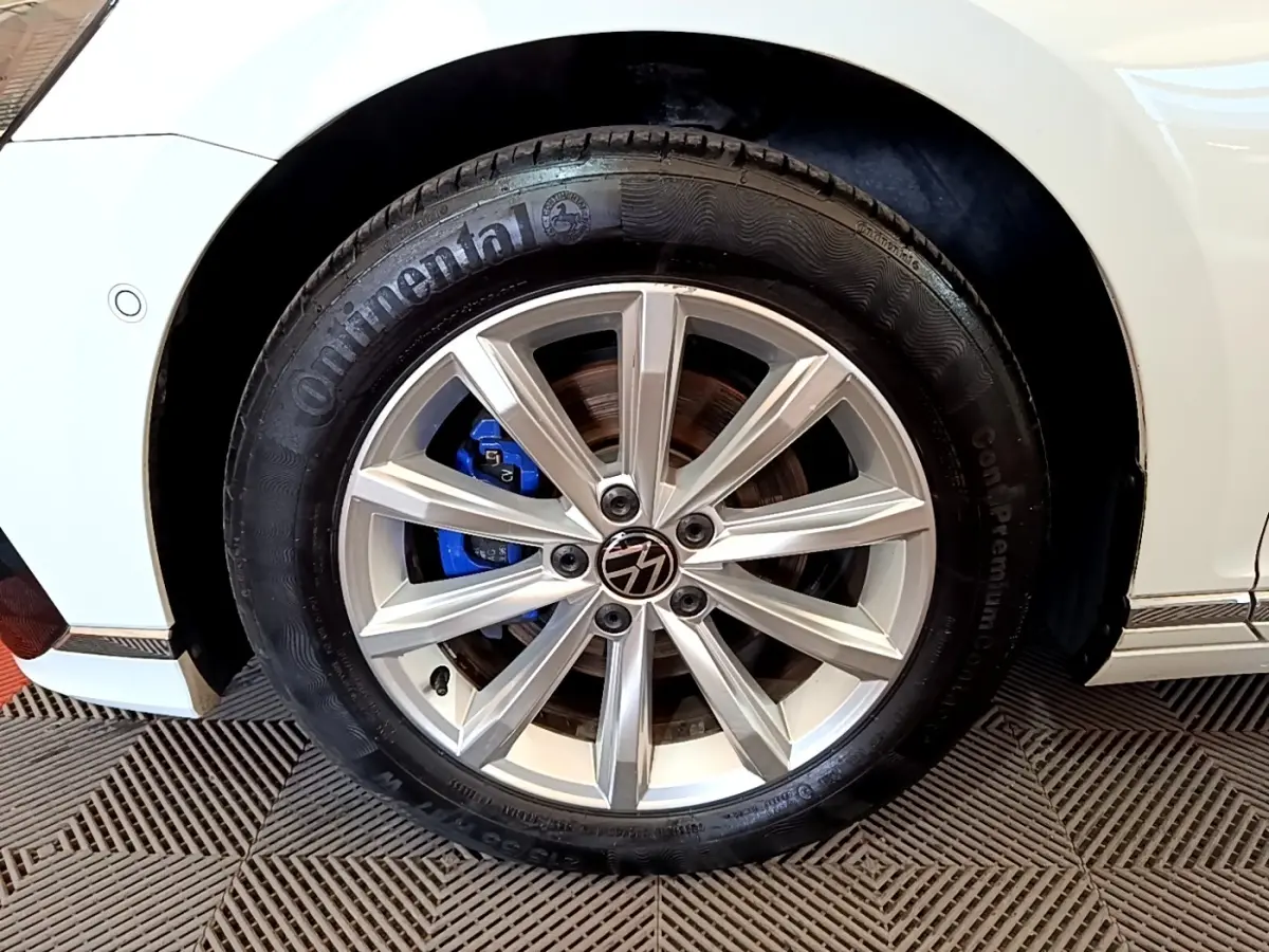 Gros plan sur la roue avant droite blanche d'une Volkswagen Passat hybride avec étrier de frein bleu visible.