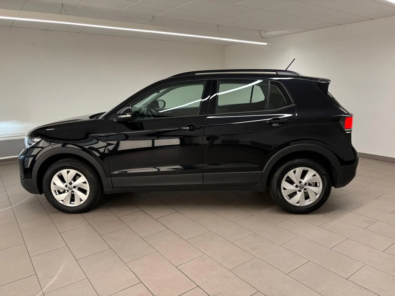 Volkswagen T-Cross 2024 noir intense vu de profil côté gauche dans un intérieur lumineux avec jantes argentées.